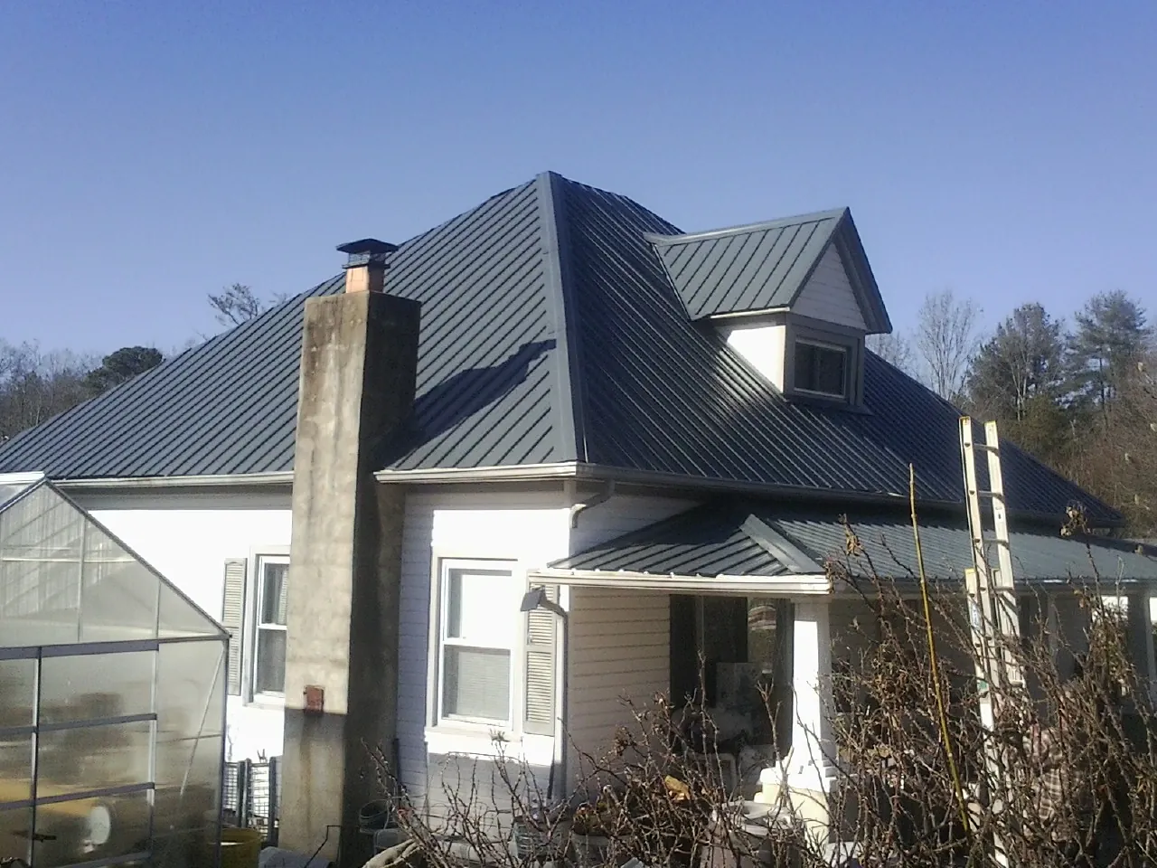 Dark blue standing seam metal roof on a white farmhouse with dormer — Slate & Tile Roof Repair by Roofing Brothers in Tarzan