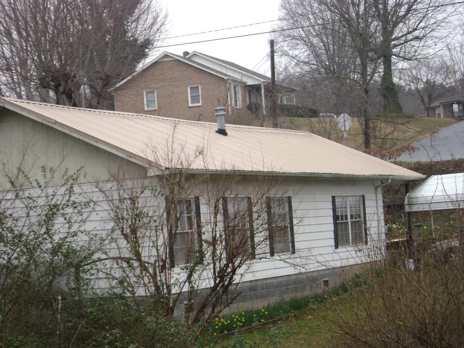 Tan metal roof on a white sided house set into a hillside — Commercial Roofing by Roofing Brothers in Tarzan